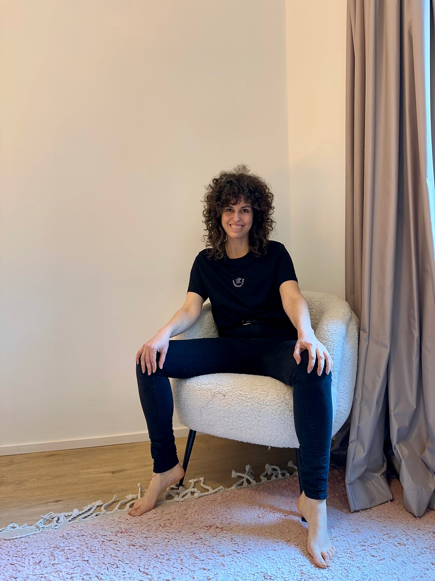 woman sitting on a chair wearing the black shirt with the small logo in the center
