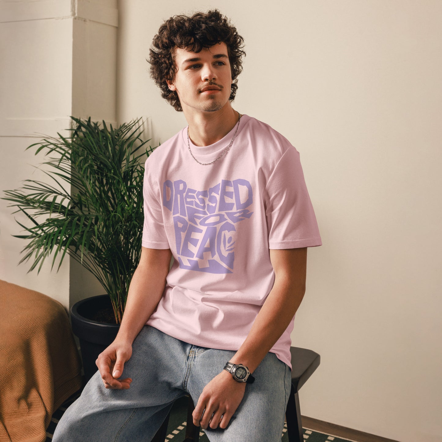 Person wearing a pink t-shirt with text, sitting indoors next to a plant.
