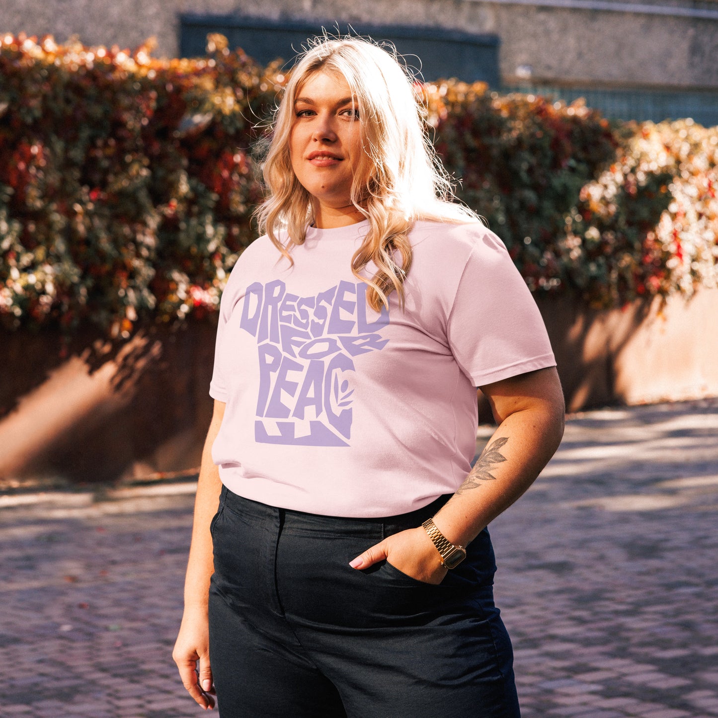 Person wearing a light pink t-shirt with purple text, standing outdoors.