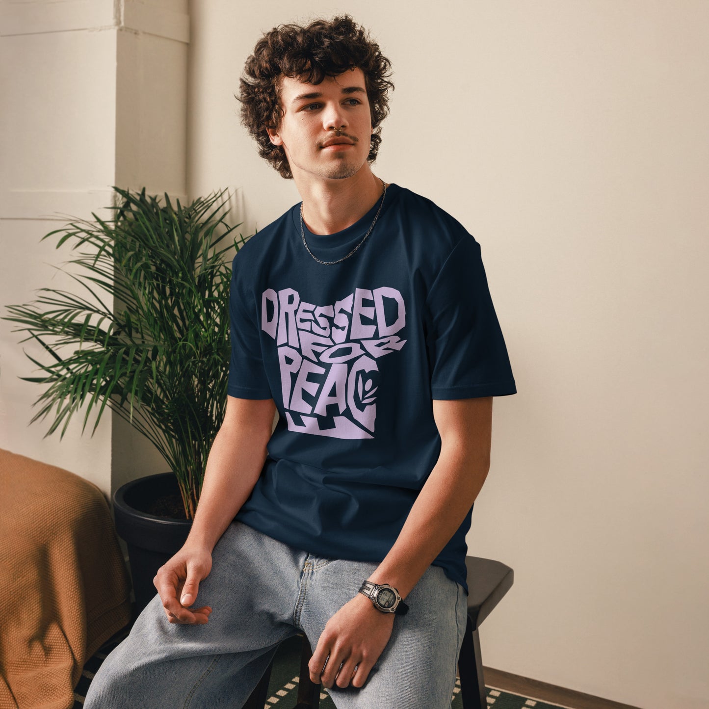 Person wearing a navy blue t-shirt with text, sitting indoors next to a plant.