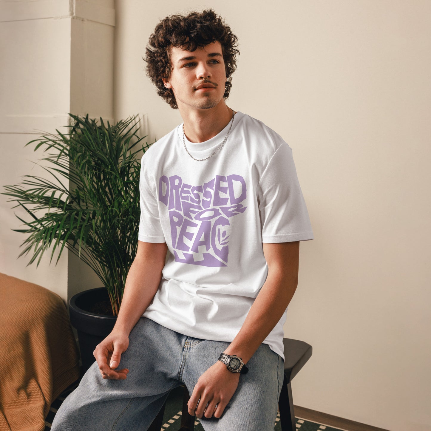 Person wearing a white t-shirt with purple text sitting indoors next to a plant.