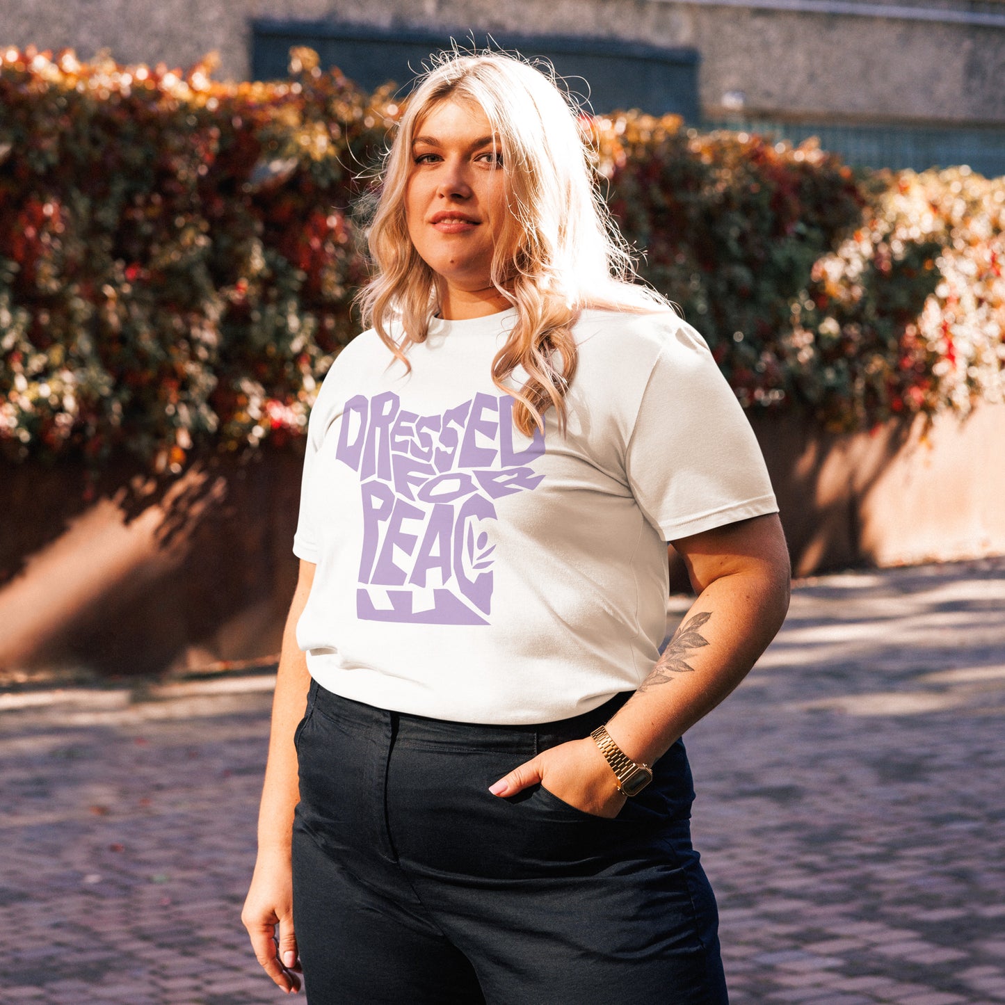Person wearing a white t-shirt with purple text standing outdoors.