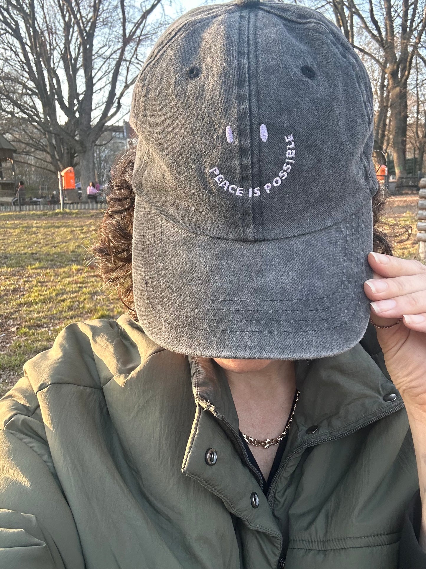 Person wearing a gray cap with 'Peace is Possible' text outdoors